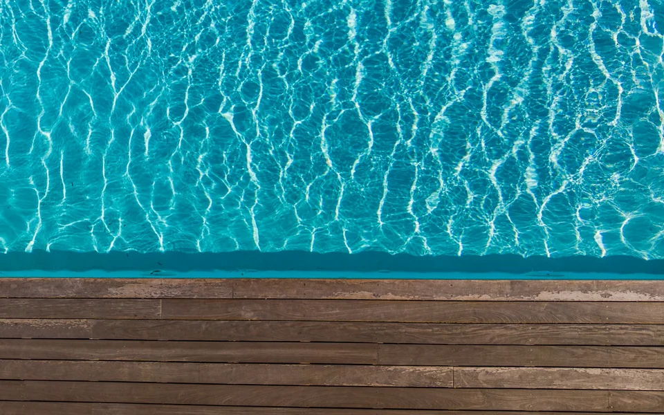 Weathered wood deck boards along the edge of a blue swimming pool
